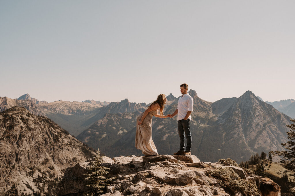 couple laughs in front of mountain peaks after surprise proposal near North Cascade National Park