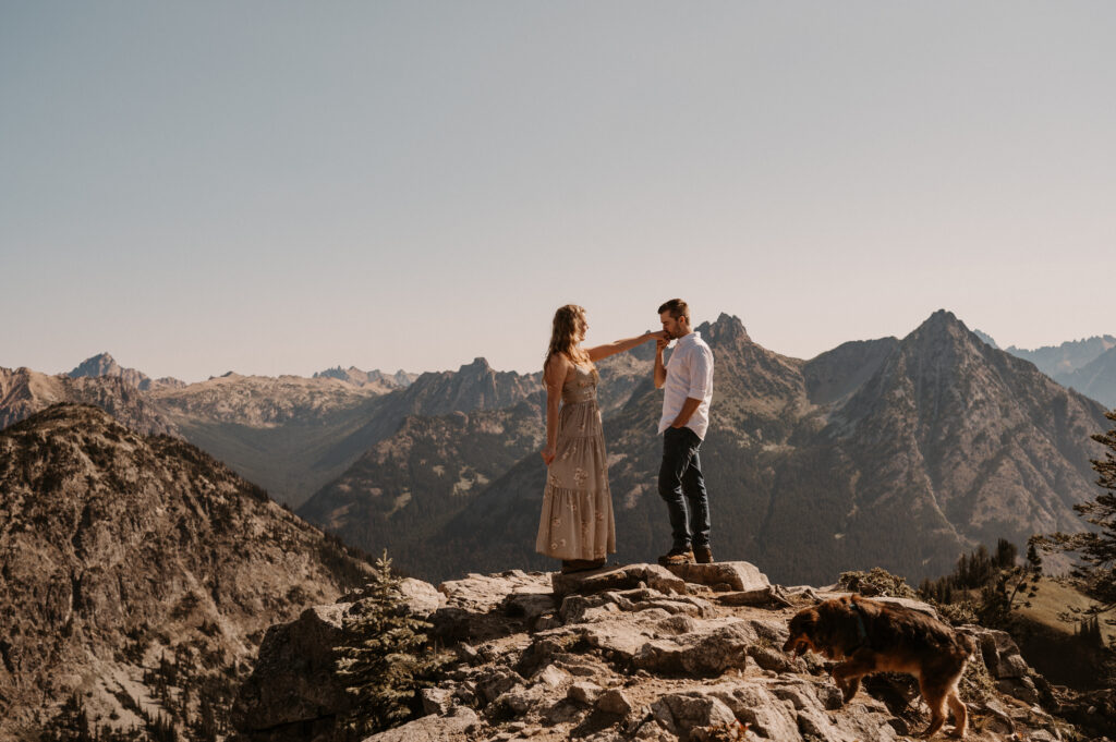 couple holds hands in front of mountain peaks after surprise proposal near North Cascade National Park