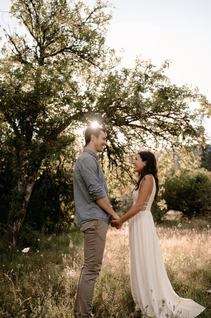 couple looks at each other holding hands while sun glows behind them 