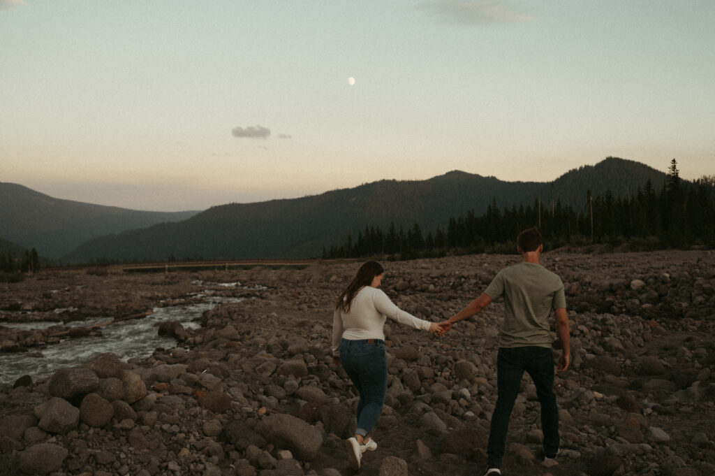 couple holding hands next to mountain river during mountain engagement