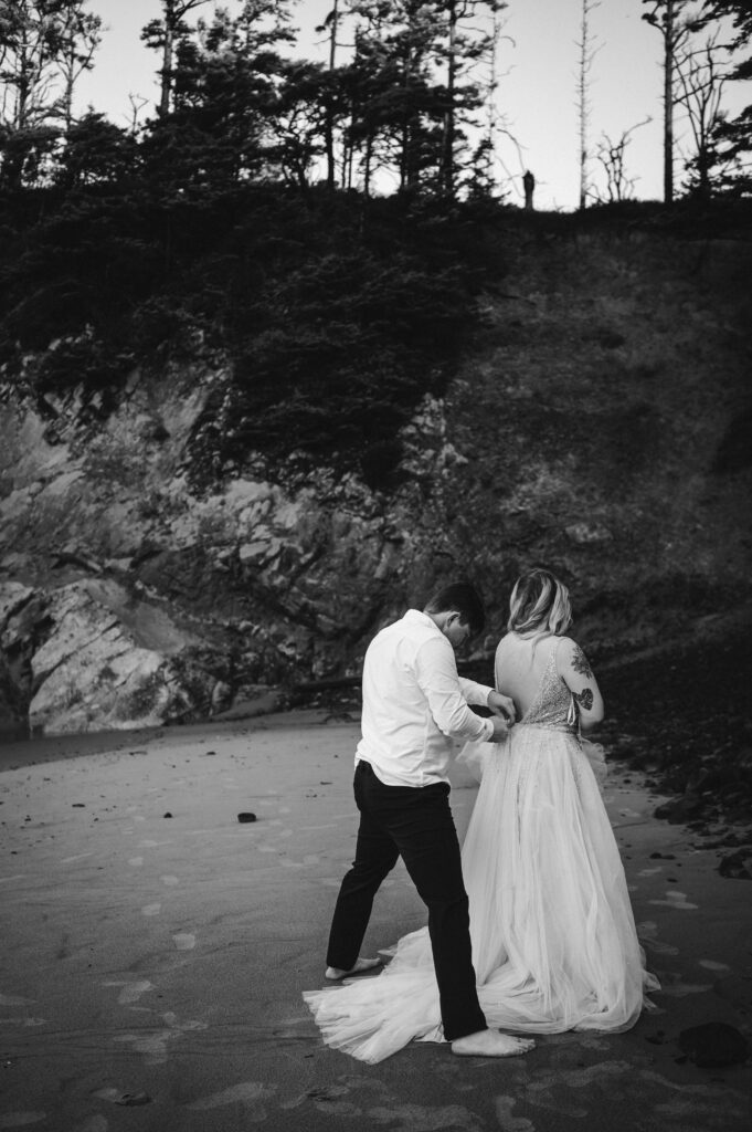 groom helps zip brides dress during their oregon coast elopement