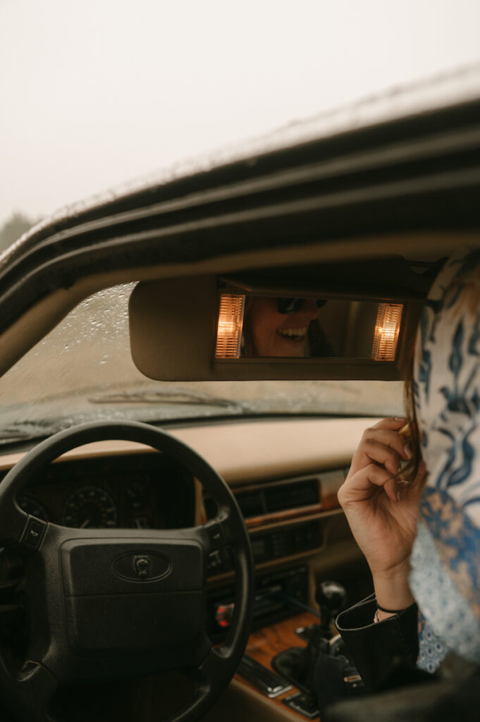 woman putting on lipstick in visor mirror of vintage jaguar