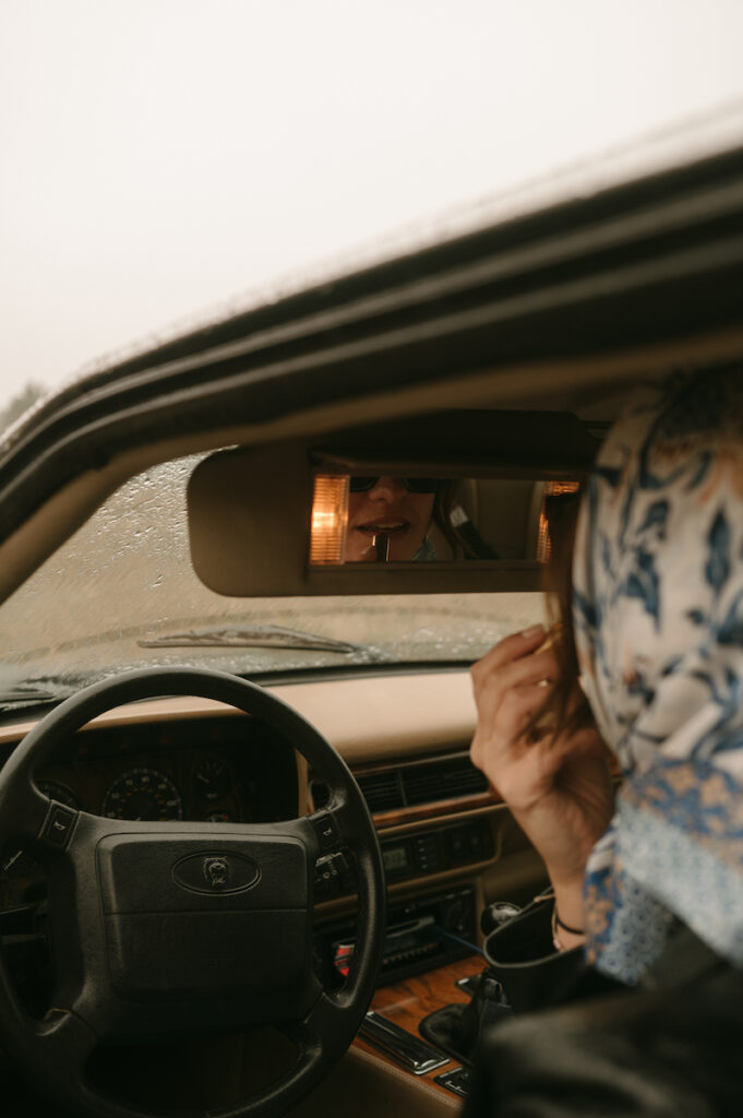 woman putting on lipstick in classic jaguar car
