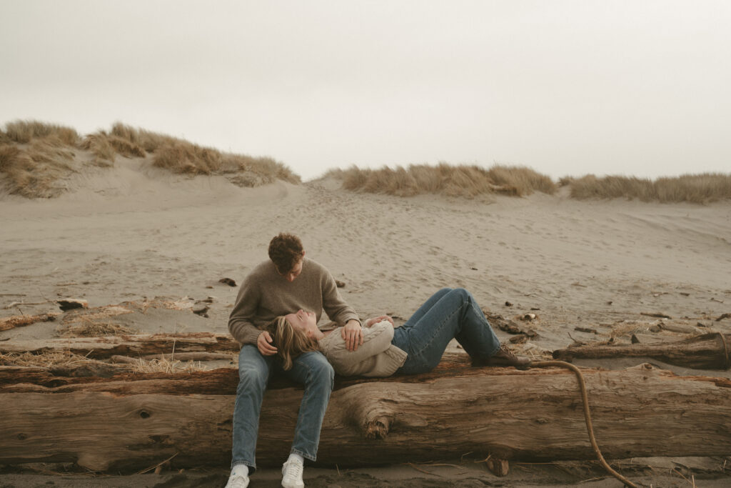 couple lays on a log during their oregon coast engagement session
