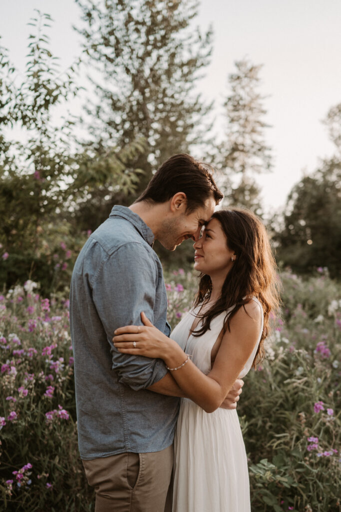 copule embraces, touching foreheads in front of pink wildflowers during engagement session in columbia river gorge