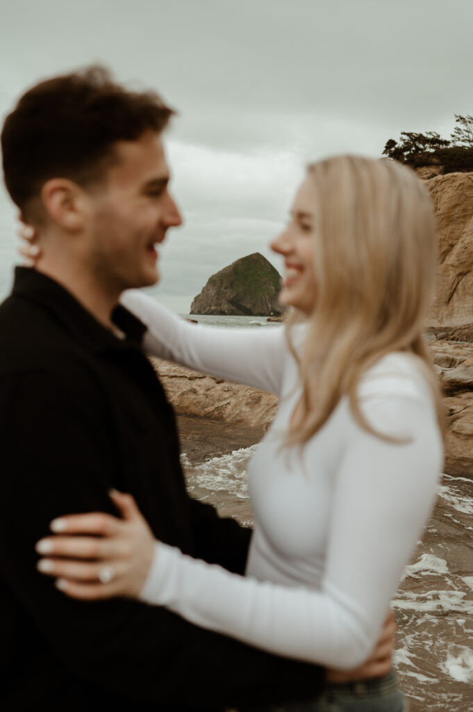 Couple embracing with Kiwanda Haystack Rock behind them