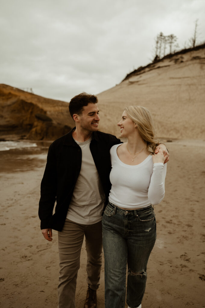 couple looking at each other while walking on the beach during their oregon coast engagement session